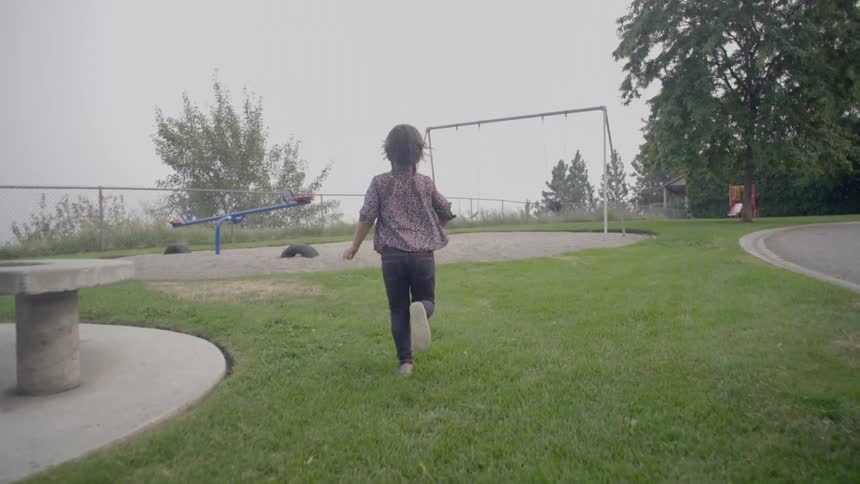 A small girl is running on the grass towards the play area