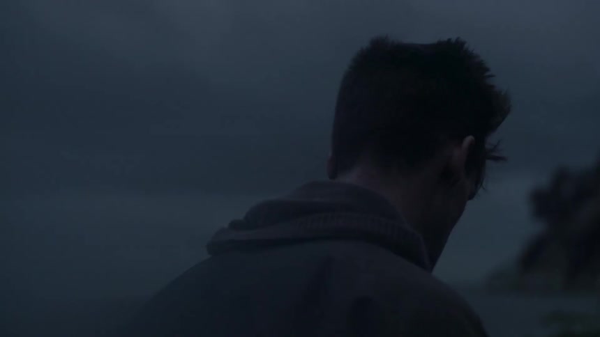 A man stands alone near the water at dusk