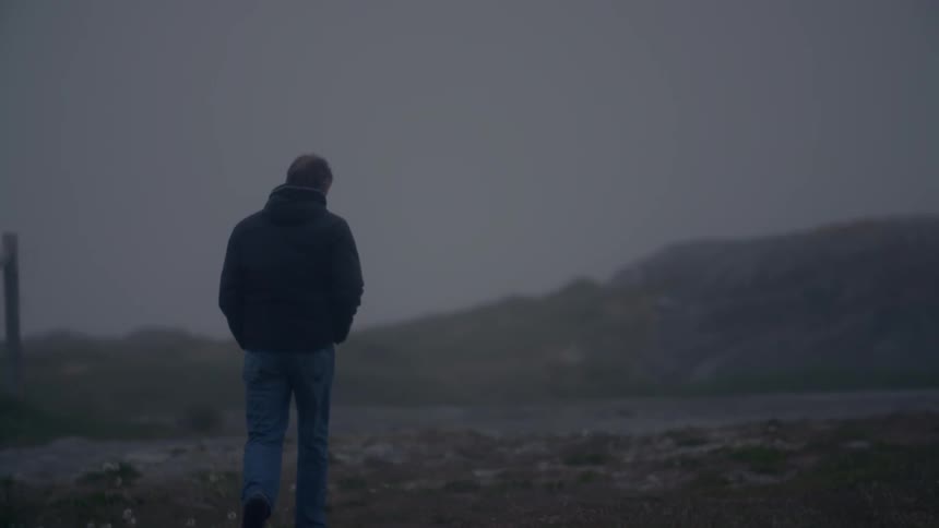 A man walks on a foggy shoreline