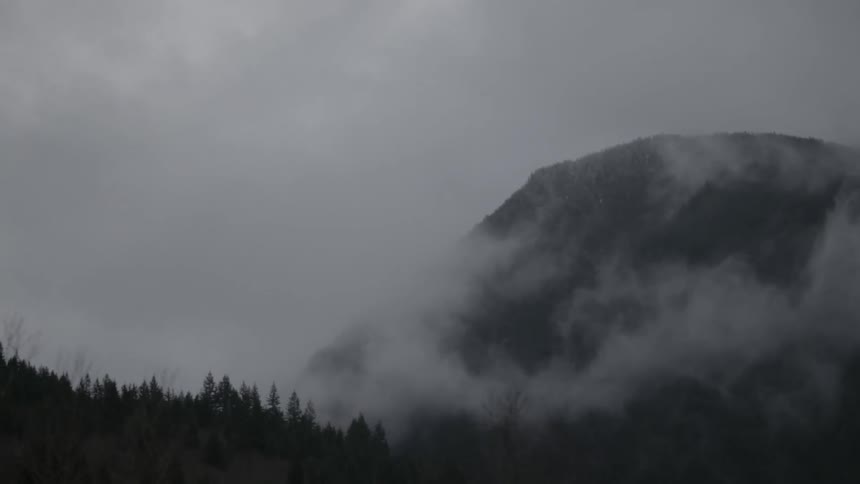 Clouds hover around a mountain in the forest