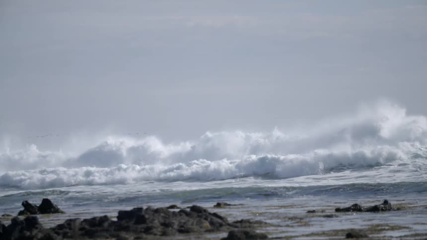 Large waves rolling in to a rocky beach on a cloudy day