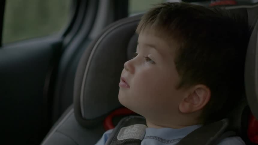 A boy rides in a car seat and looks out the window