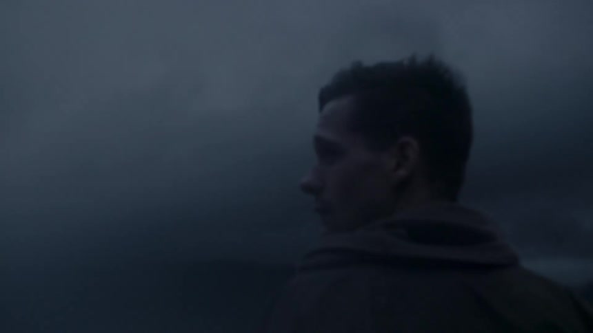 A man with short, dark hair walking through the fog
