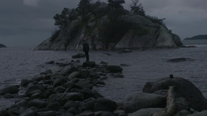 A person is outside in the outdoors standing on a rock by the water