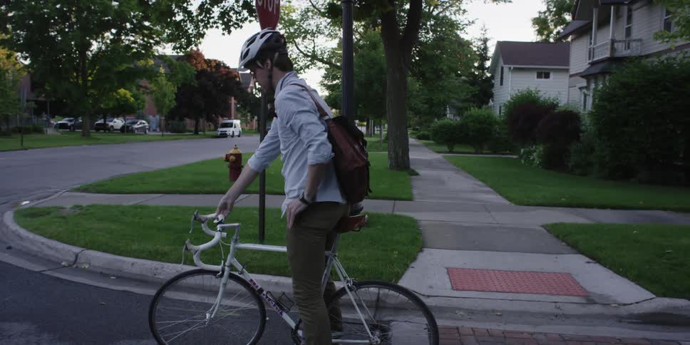 A man on a bicycles stops at an intersection and looks both ways for traffic, then pulls out his phone while he waits