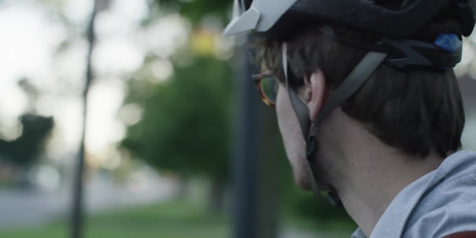 An unshaven man wearing a bicycle helmet and glasses looking towards his right and then left side
