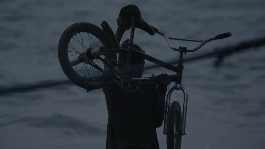 A man holding his bicycle is standing by the sea shore