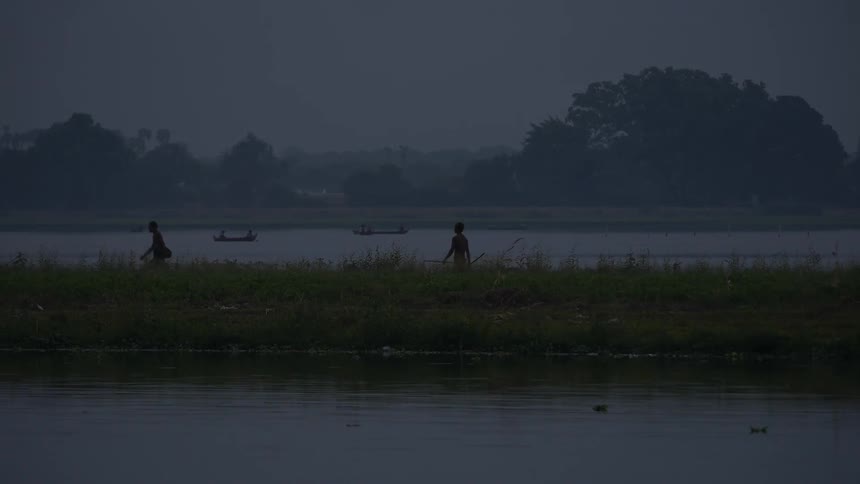 People walk through the tall grass near a river bank