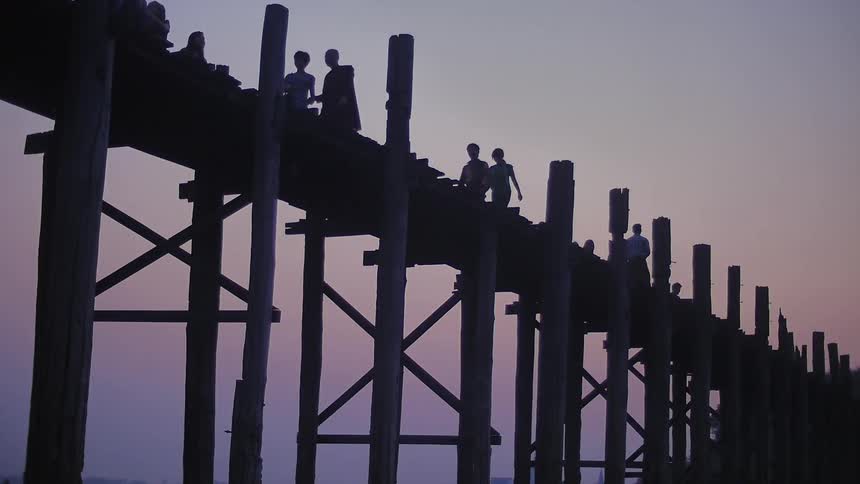 People walk across a wooden bridge at dusk