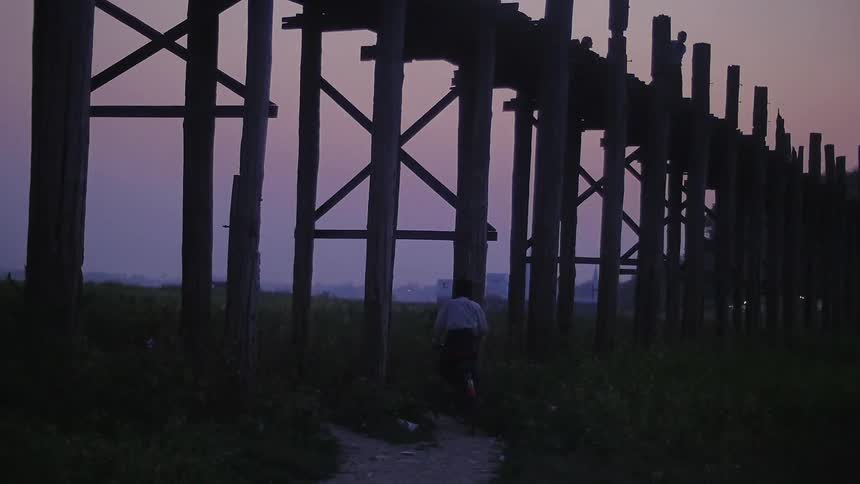 A man bicycles towards a wood bridge