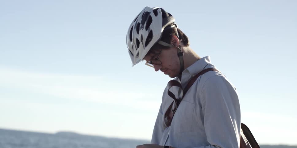 Standing with his bicycle next to a large body of water, a man looks down checking his cell phone