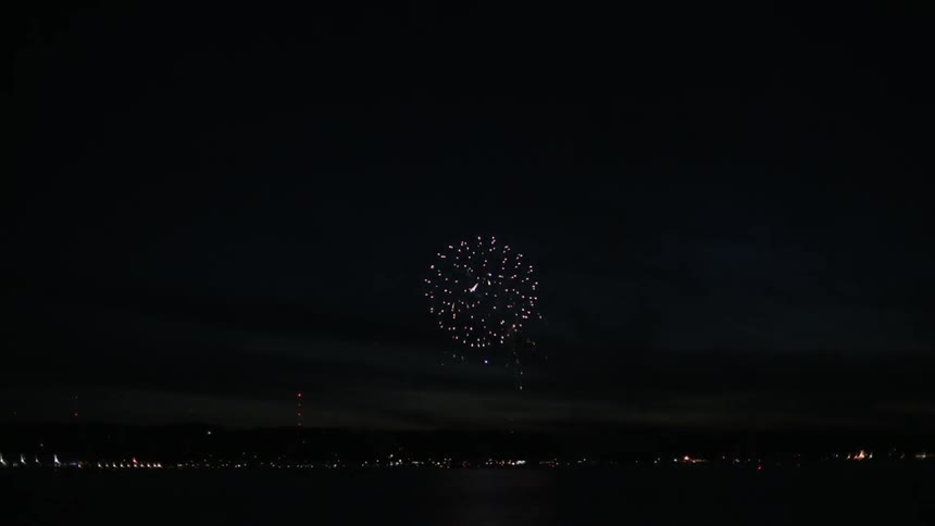 Fireworks explode over a lake in the night sky