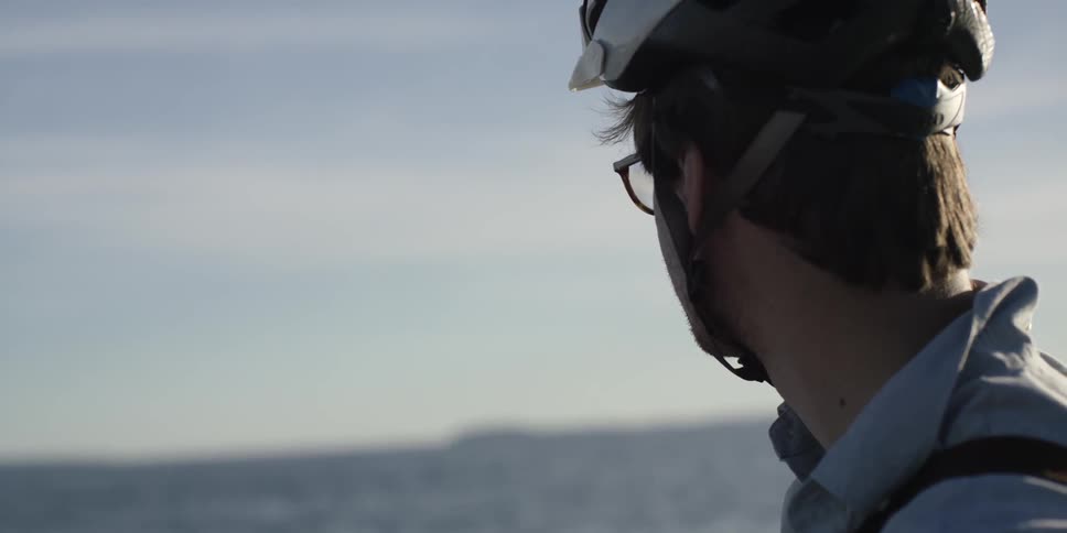 A man with a bicycle helmet looks out towards the ocean