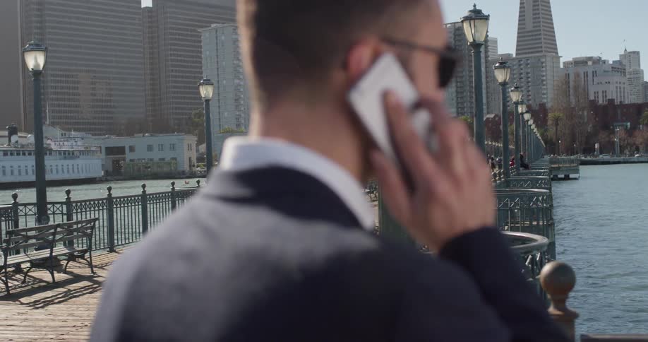 A man talks on the phone while standing on a city pier