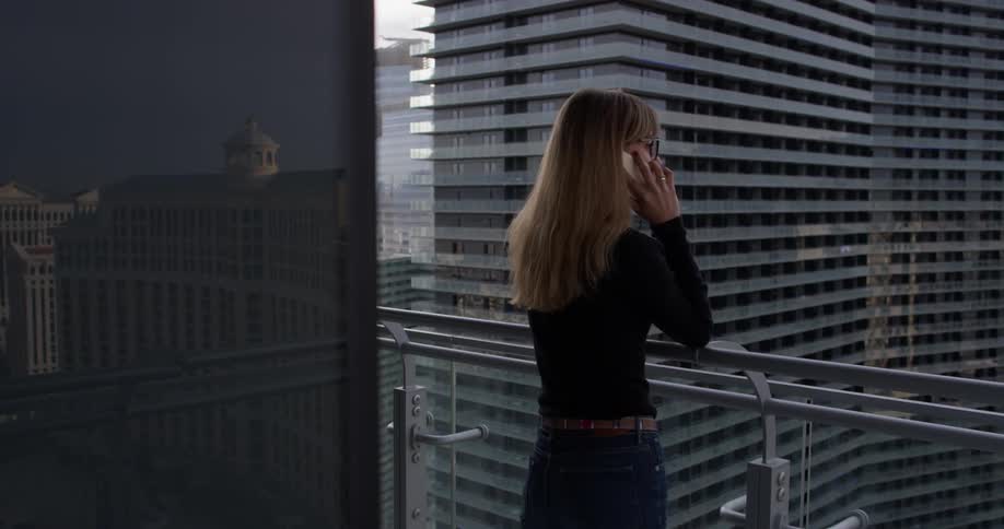 A woman talks on a phone on an apartment balcony