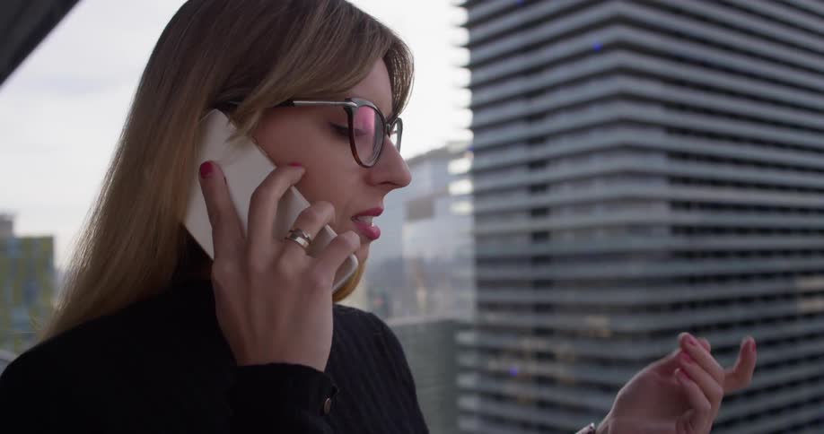 A woman talks on a phone on an apartment balcony