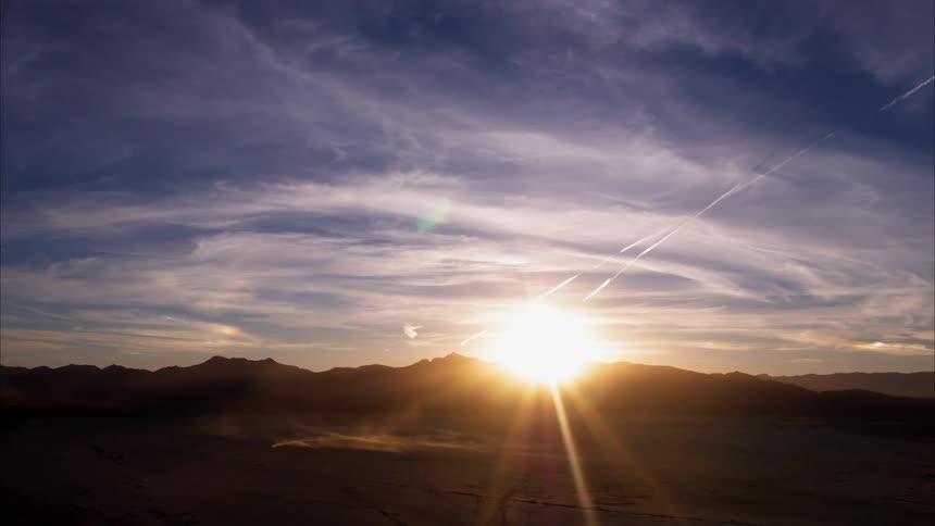 A car is kicking up dust in a desert landscape at sunrise