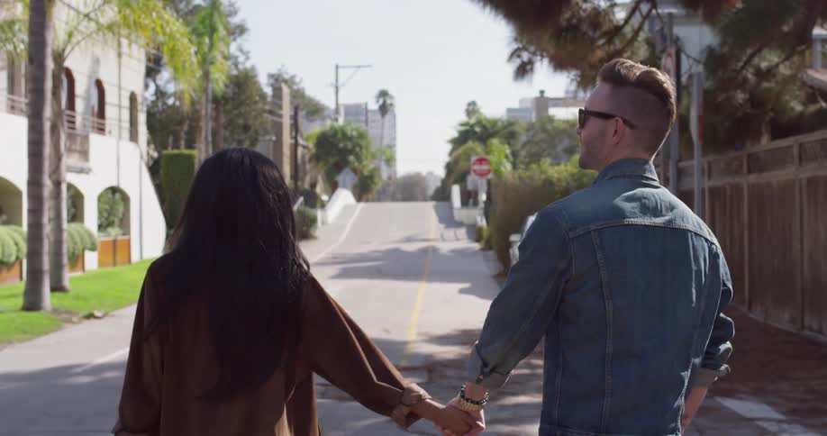 Man and woman hold hands and walk on a sunny city street