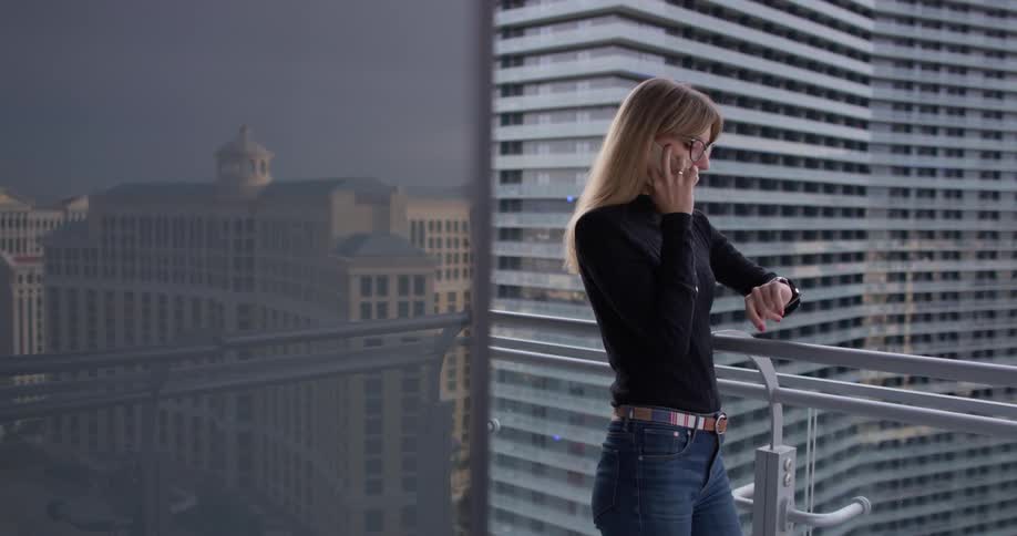 A woman is standing on a balcony and talking on a cellphone in a city in daylight