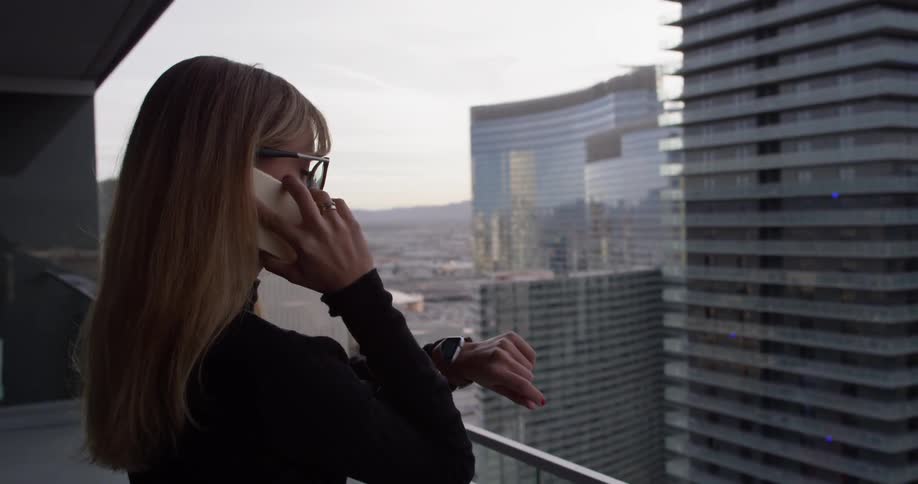 Woman talks on a phone and stands on a balcony overlooking a city