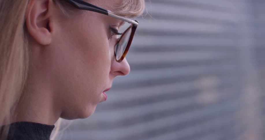 Woman wearing glasses stands outside and looks down