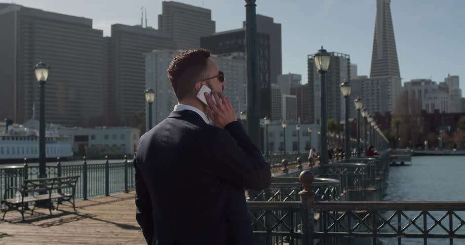 A man answers his phone outside by the water