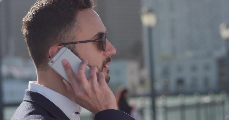 Man wearing sunglasses holds a cellphone to his ear as he talks