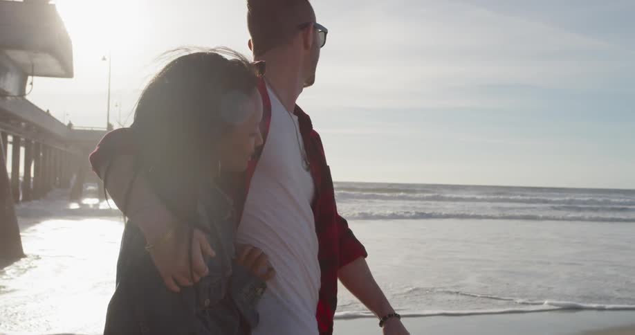 A man and woman hug as they walk on the beach