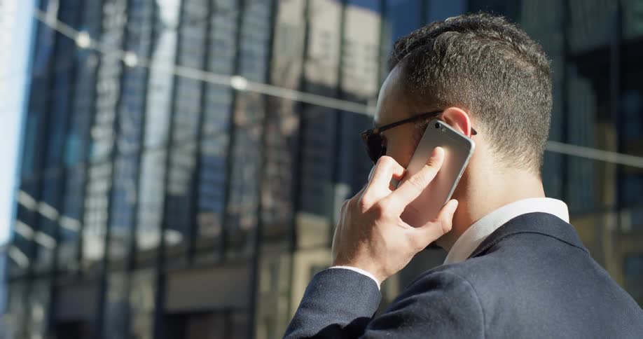 A man is standing outside in a city talking on a cellphone in daylight