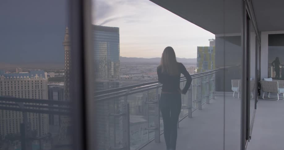A woman talks on a phone on an apartment balcony