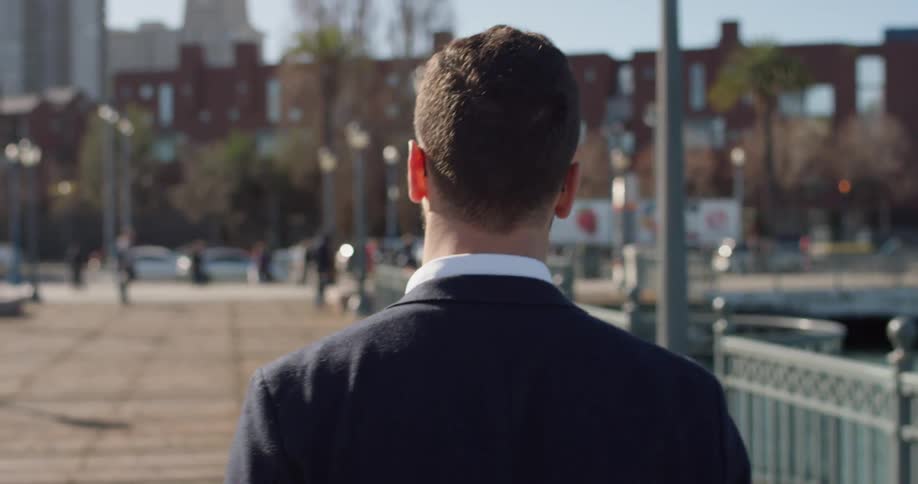 Man wearing sunglasses walks near a fence in the city