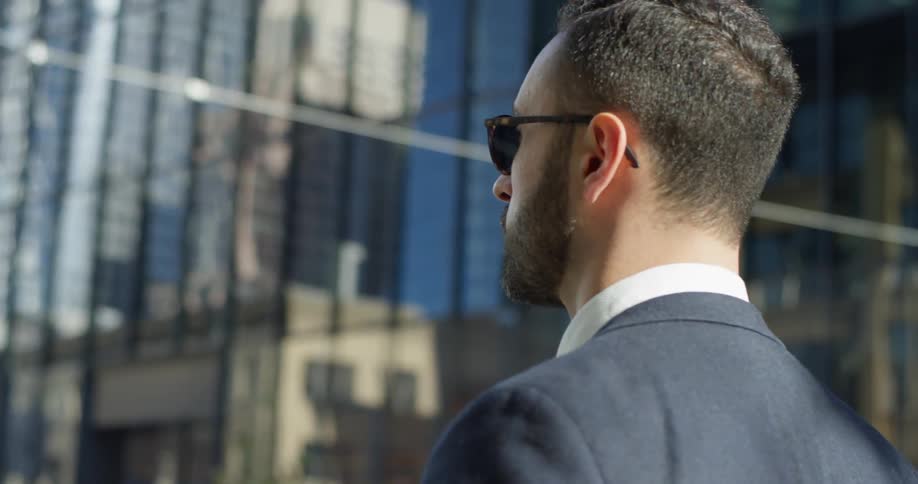 A man in a suit stands outside of a glass building