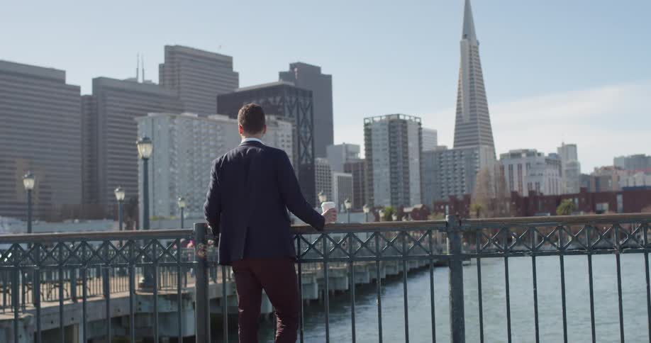 Man leans against a railing overlooking a river next to a city'