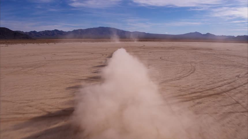 Car drives on large flat dusty area of land