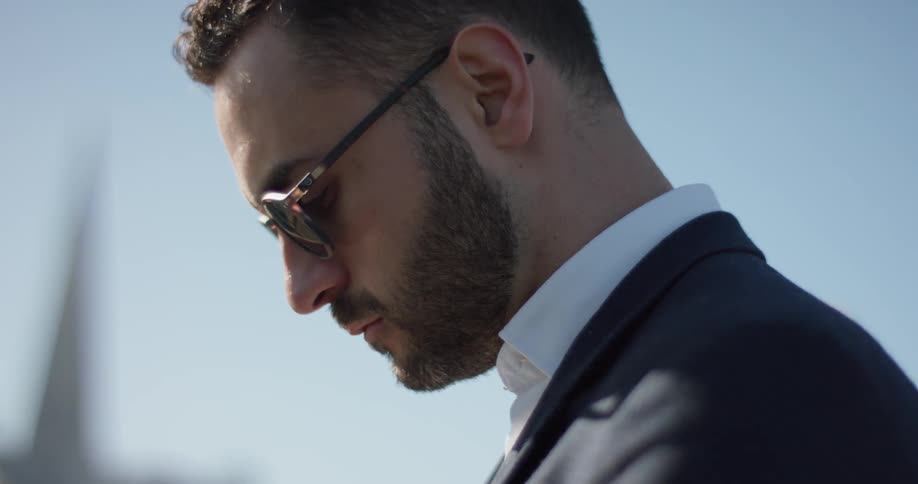 A man in a suit wears sunglasses outside