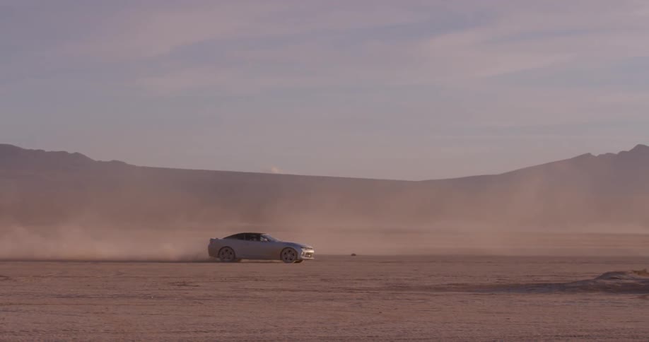 Car drives on large flat dusty area of land