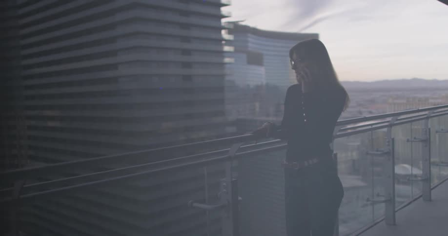 Woman is talking on phone on balcony in city