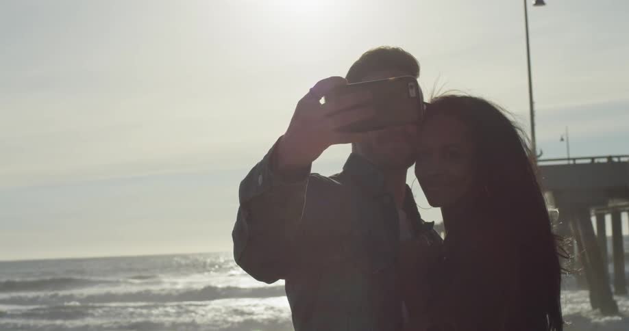A man and woman take a photo together on the beach