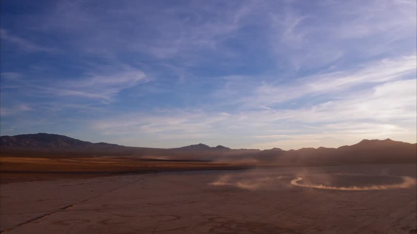 A car spins in circles in a dirt field surrounded by mountains