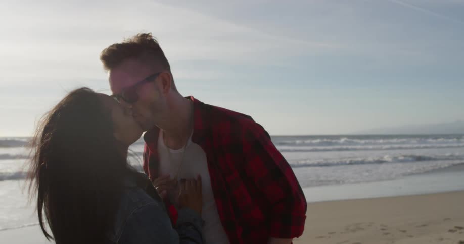 A man and woman kiss on the beach