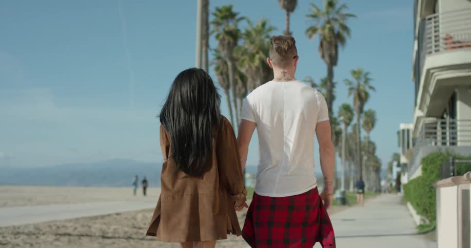 A man and woman hold hands as they walk by the beach