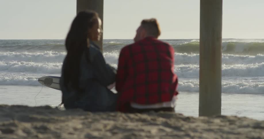 Man and woman sit in the sand talking near the ocean