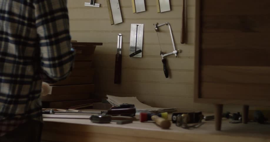 A man approaching a workbench that is full of tools and picking up some of the tools
