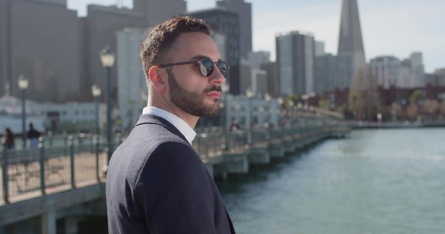 Man wearing sunglasses stands near the lake and looks around