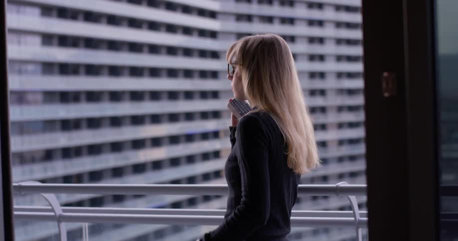 Woman is talking on cell phone on balcony in city
