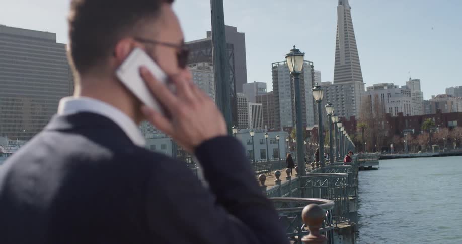 A man in a suit answers his phone by the water