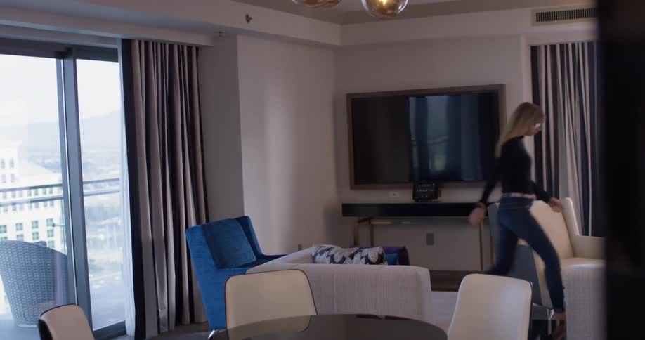 A woman walks and sits down on a living room chair to use a laptop