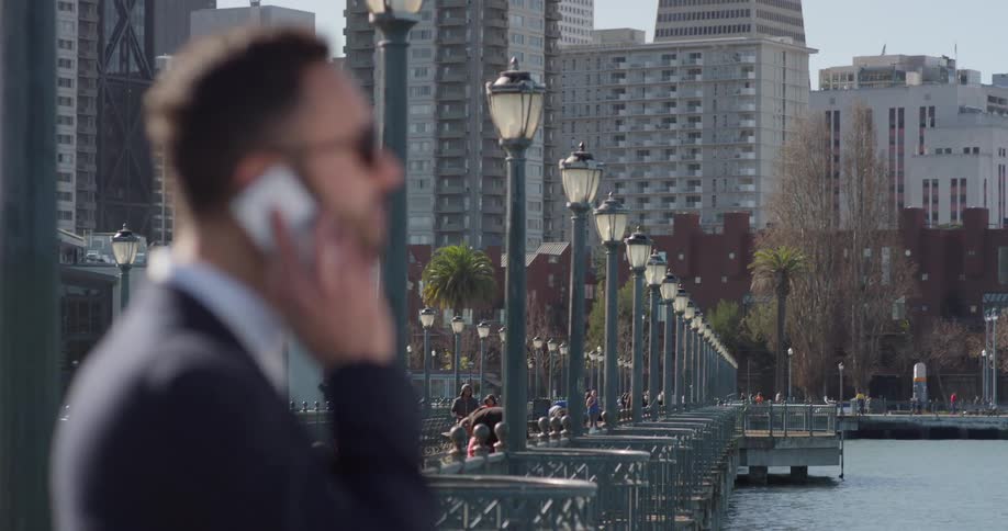 Man wearing sunglasses holds a cellphone to his ear in the city