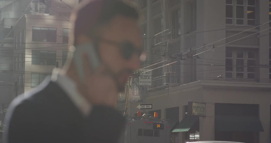 A man talks on a phone on a city sidewalk