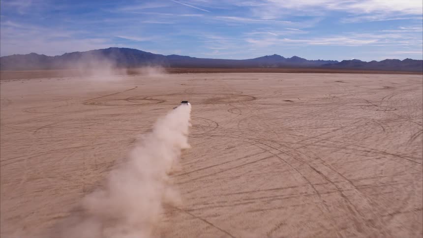 A car kicks up dirt as it speeds across the open land